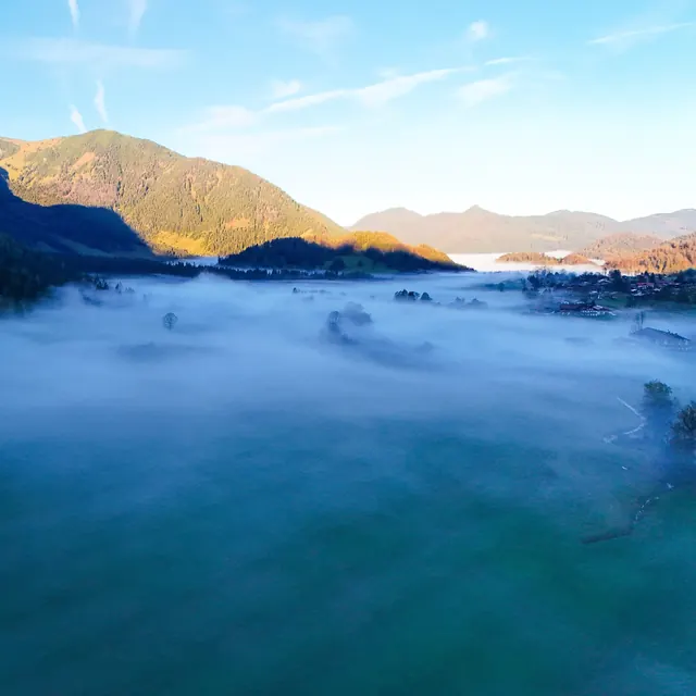 Bodennebel über einem See vor bewaldeten Berghängen