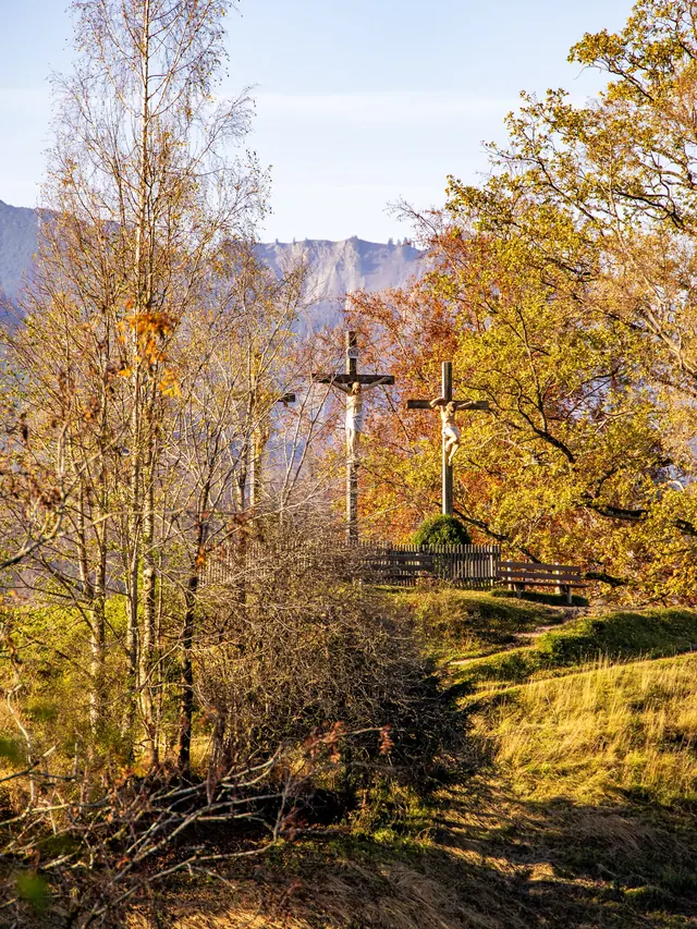 Zwei Holzkreuze zwischen herbstlich gefärbten Bäumen auf einer Anhöhe